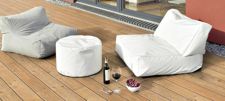 Holzterrasse mit bequemen Sitzsäcken, weißem Pouf und stilvoll arrangiertem Wein und Snacks.