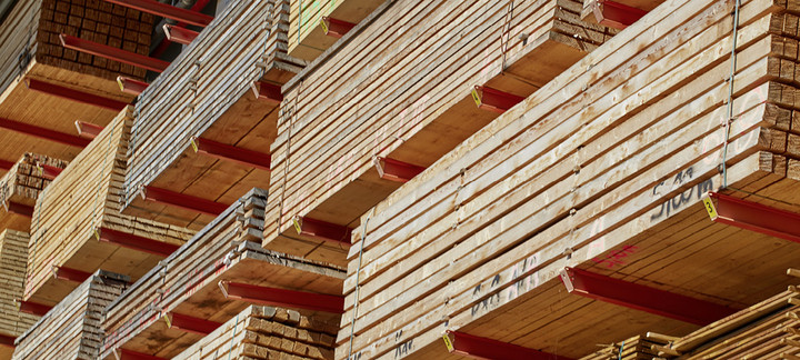 Gestapeltes Bauholz in einem Lagerregal mit roten Trägern, bereit für den Holzbau und die Weiterverarbeitung.